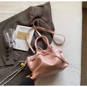 Detail der rosa glänzenden Falten-Eimertasche mit Schleifen-Kordelzug und Pompon-Anhänger