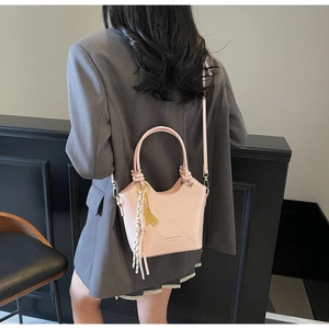 Detalle de bolso bucket de charol rosa con borla y herrajes dorados sobre blazer gris