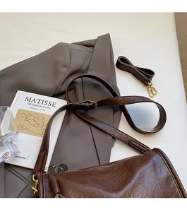 Detail of vintage brown leather crossbody bag with gold hardware on grey suit fabric