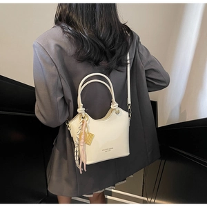 Detalle de bolso cubo de cuero encerado crema con colgante trenzado y logotipo dorado