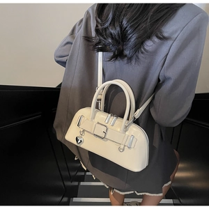 Détail du sac bowling beige rétro avec pendentif cœur porté sur un blazer gris
