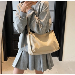 Detail view of cream canvas tote bag with black woven label shown in casual wear use