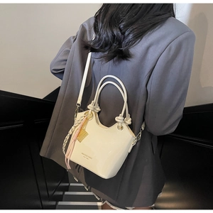 Detalle del bolso de cubo crema con asas anudadas y colgantes sobre un blazer gris