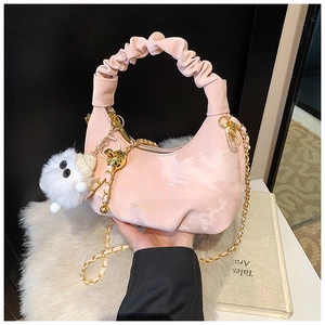 Gros plan du sac froncé rose avec chaîne dorée et breloque pompon en peluche blanc