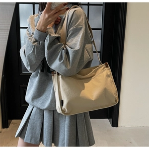 Close-up of beige canvas pillow bag with wide shoulder strap and woven side label