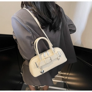 Détail du sac bowling en cuir blanc cassé avec pendentif cœur porté par un modèle