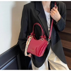 Detalle del bolso de mano en piel charol roja con logo dorado y colgante de borla a rayas