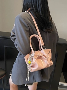 Rosa plissierte Beuteltasche mit Schleife an Model im grauen Blazer mit Anhängern