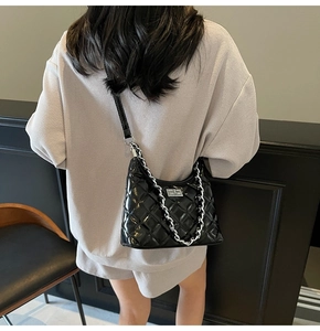 Detail of black quilted leather shoulder bag with silver chain and turn-lock on a model