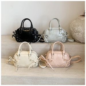 Quatre sacs Boston à nœud papillon en noir, argent, beige et rose exposés sur des marches