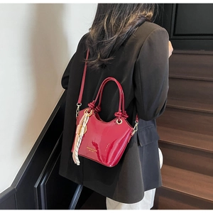 Detalle de bolso bucket de cuero encerado rojo con pañuelo de seda y logo dorado lateral