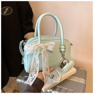 Détail du sac polochon bleu clair avec nœud en dentelle blanche et pendentif en cœur