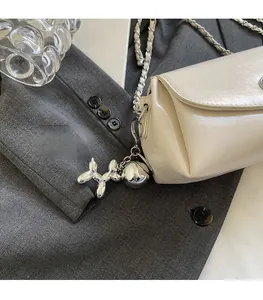 Detail of cream crossbody bag featuring a silver chain strap and balloon dog charm