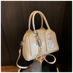 Detail of cream glossy Boston bag with a cartoon corgi card and woven charm strap