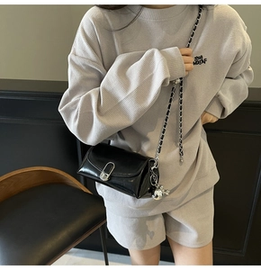 Detail of black glossy chain bag with silver oval lock worn by model in gray outfit