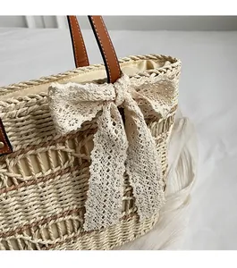 Detail of woven straw tote bag featuring a large white lace bow and brown leather handle