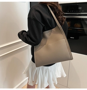 Detail view of large taupe lychee grain leather tote bag on model in a modern room