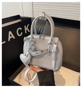 Detail of light grey shell bag featuring a matte leather finish and heart charm