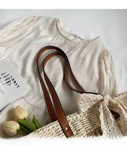 Detail of sturdy brown leather shoulder strap on a beige woven straw tote bag