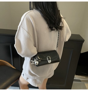 Detail of black glossy crossbody bag with silver twist lock and chain strap on shoulder