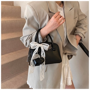 Detail showing shiny black leather handbag with white lace bow and heart pendant charm