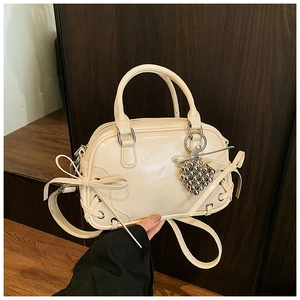Détails du sac Boston crème avec nœud décoratif, fini brillant et breloque métallique