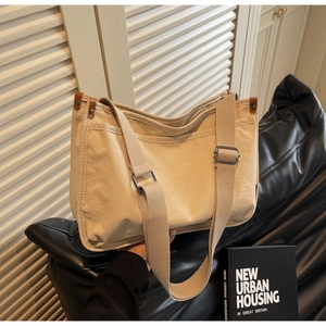 Detail of beige canvas tote bag featuring brown leather trim and adjustable strap