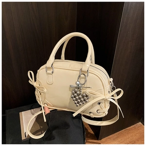 Détails du sac Boston crème avec des nœuds élégants et un pendentif cœur argenté