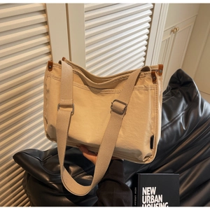 Detail of beige canvas tote bag showing wide shoulder straps and brown leather buckle