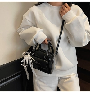 Detail of black glossy handbag featuring lace pearl bow charm and magnetic flap pocket
