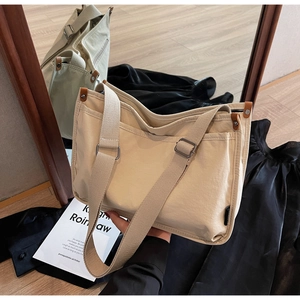 Detail of beige canvas tote bag with adjustable wide strap and brown leather accents