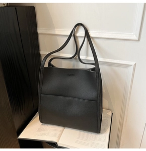 Close-up of black lychee grain leather tote bag with elegant stitching on an art book