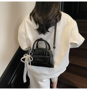 Detail of glossy black leather handbag with chic bow accent and lace pearl charm
