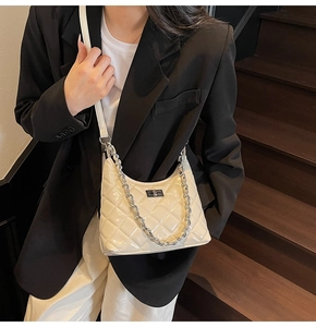 Detail of white quilted patent leather bag with silver chain strap on a dark staircase