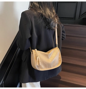 Close-up of beige shoulder bag featuring soft pleated texture and stylish fringe zipper detail