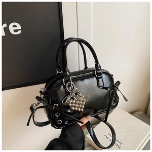 Détail du sac Boston en similicuir verni noir avec nœud et pendentif cœur