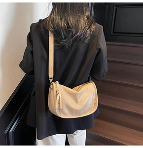 Detail showing beige hobo bag with leather texture and fringe zipper pull on a model