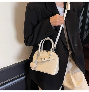 Detail of cream patent leather shell bag with heart charm and detachable shoulder strap