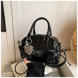 Détail du sac Boston noir brillant avec breloque cœur argentée et nœuds latéraux