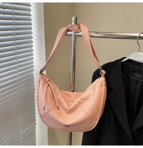 Détail du sac demi-lune rose avec logo argenté, cordon à pompons et bandoulière large