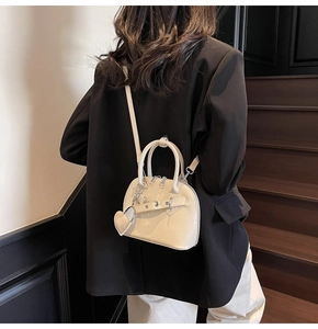Detail view of cream patent leather shell bag with heart charm and silver chain strap