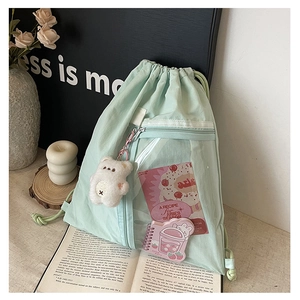 Detail of light green drawstring backpack with clear pocket and plush bear pendant