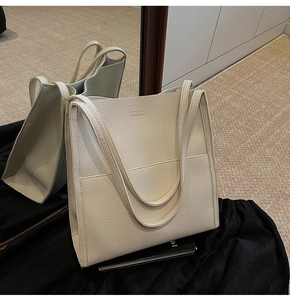Detail of the cream pebbled leather tote bag with a minimalist logo and front pocket