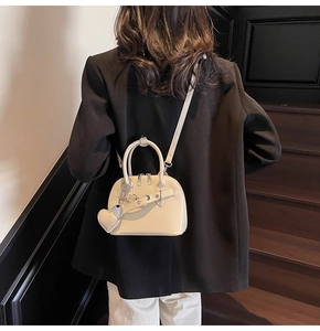 Detail of a creamy white shell bag with glossy finish and heart pendant decoration