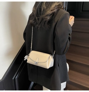 Detail of cream flap crossbody bag with silver chain and rabbit charm on model