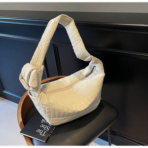Detail of off-white quilted nylon shoulder bag with decorative knotted strap on chair