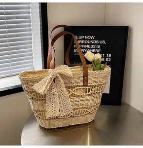 Detail of beige straw tote bag featuring a large lace bow and brown leather handles