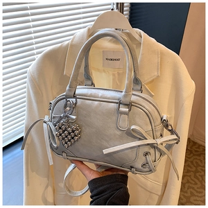 Détail du sac Boston gris avec noeud et pendentif coeur sur un blazer blanc