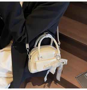 Detail of cream bowling bag with bow pocket and lace pearl charm on model