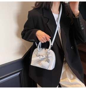 Detailed view of a white shell bag featuring a heart charm and crossbody strap worn by a model